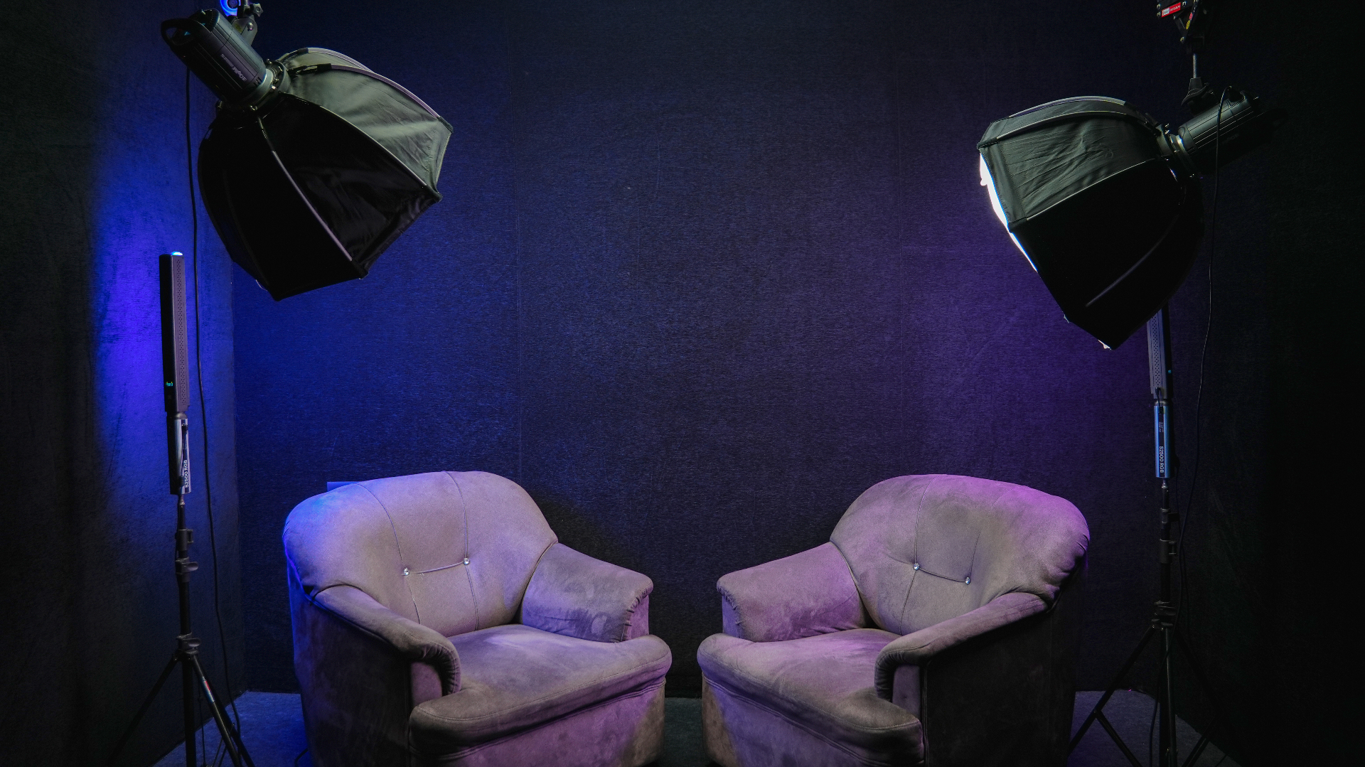 Podcast setup with two armchairs, softbox lights and dark studio backdrop